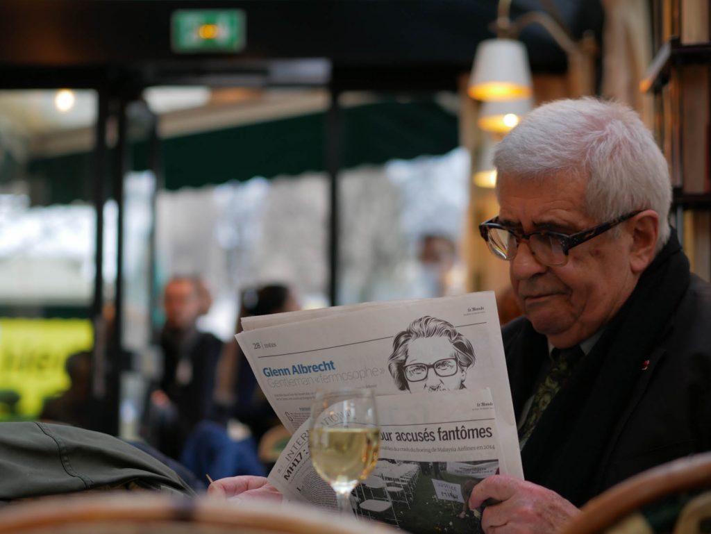 Man sitting at a Parisian café reading newspaper