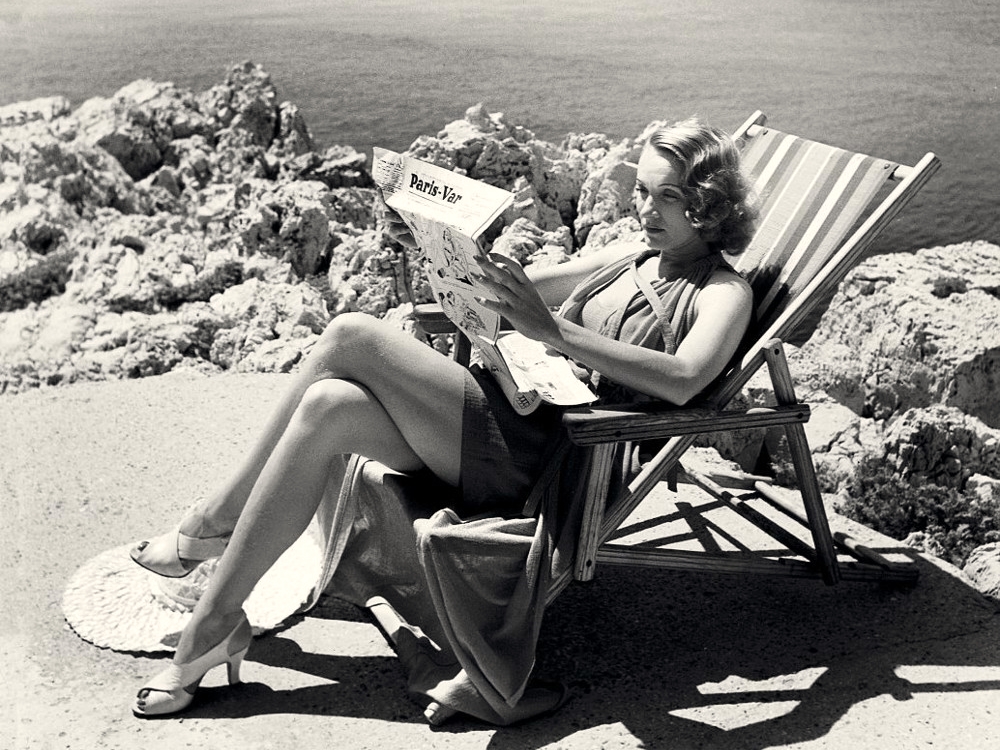 Marlene Dietrich reading newspaper on a sun lounger.